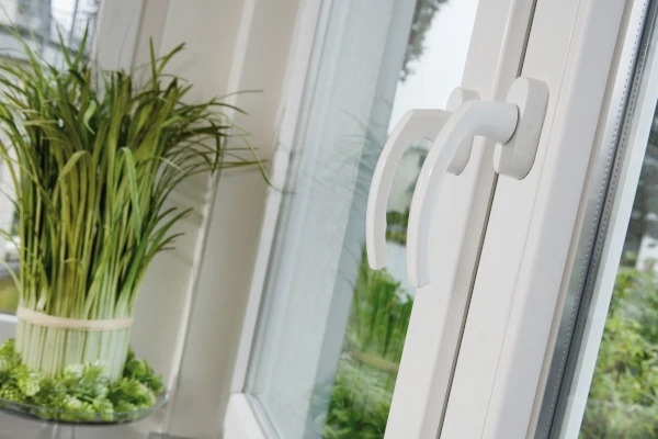 Detailaufnahme eines weißen WIRUS Fensters mit ergonomischem Griff im Fokus; im Hintergrund eine helle Wohnumgebung mit dekorativer Pflanze auf der Fensterbank.